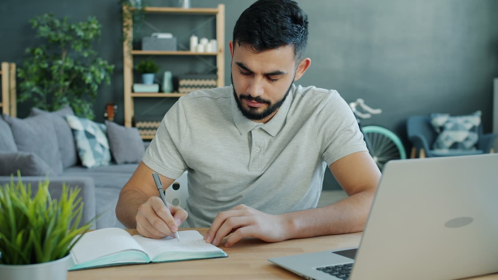 A person writing in a notebook next to a laptop.